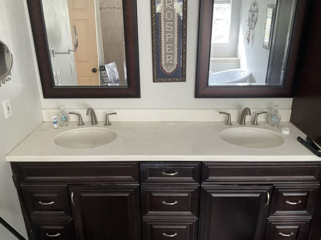 Double bathroom vanity with two chrome widespread faucets set in a cultured marble top over dark wood cabinets