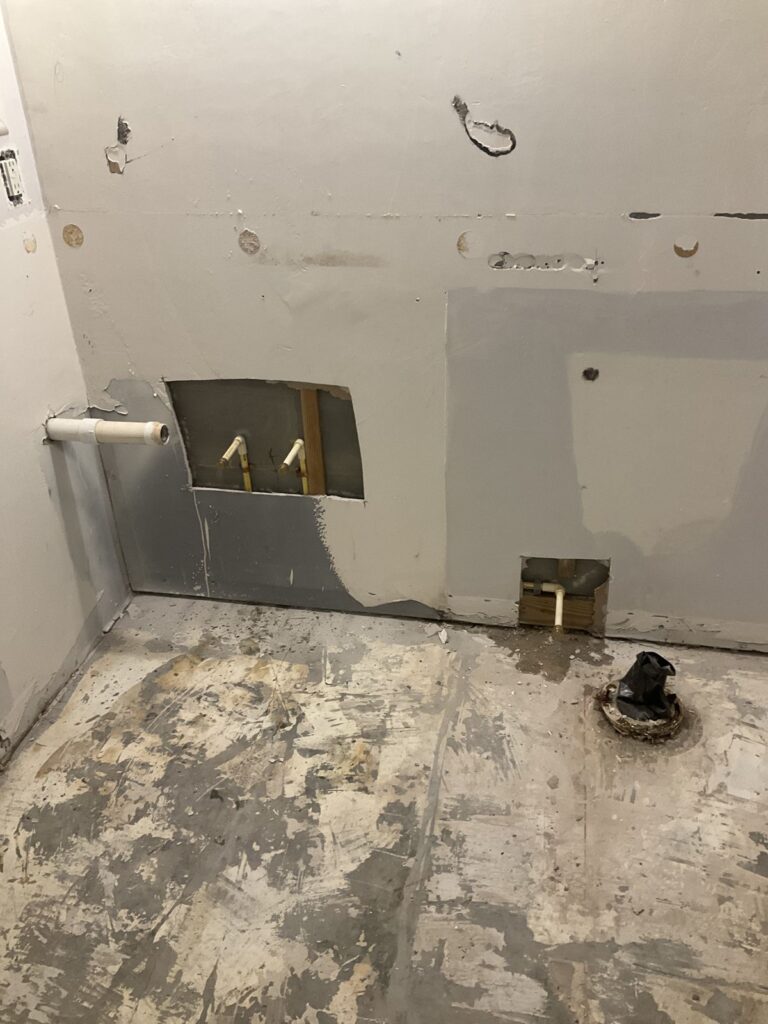 Bathroom wall with a patched opening, capped supply stubs, a drain stub and a toilet flange