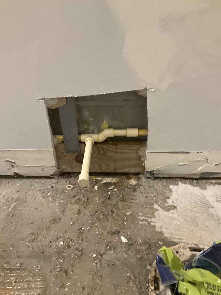CPVC water line and a white PVC drain stub at a cut wall opening above a bare floor