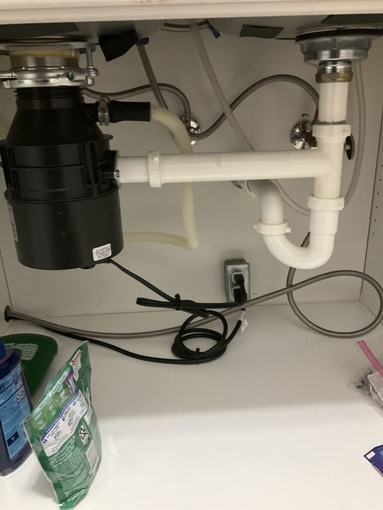 Garbage disposal with PVC double bowl waste arm, P-trap and dishwasher hose under a kitchen sink