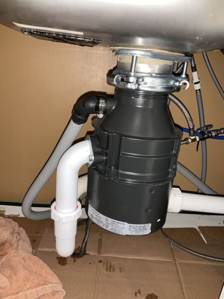 New garbage disposal under a stainless sink with the trap and dishwasher hose connected