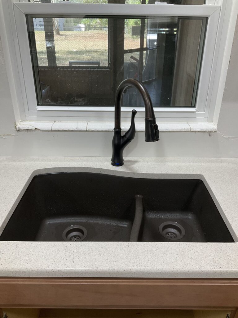 Dark bronze pull down kitchen faucet on a composite granite double bowl sink under a window