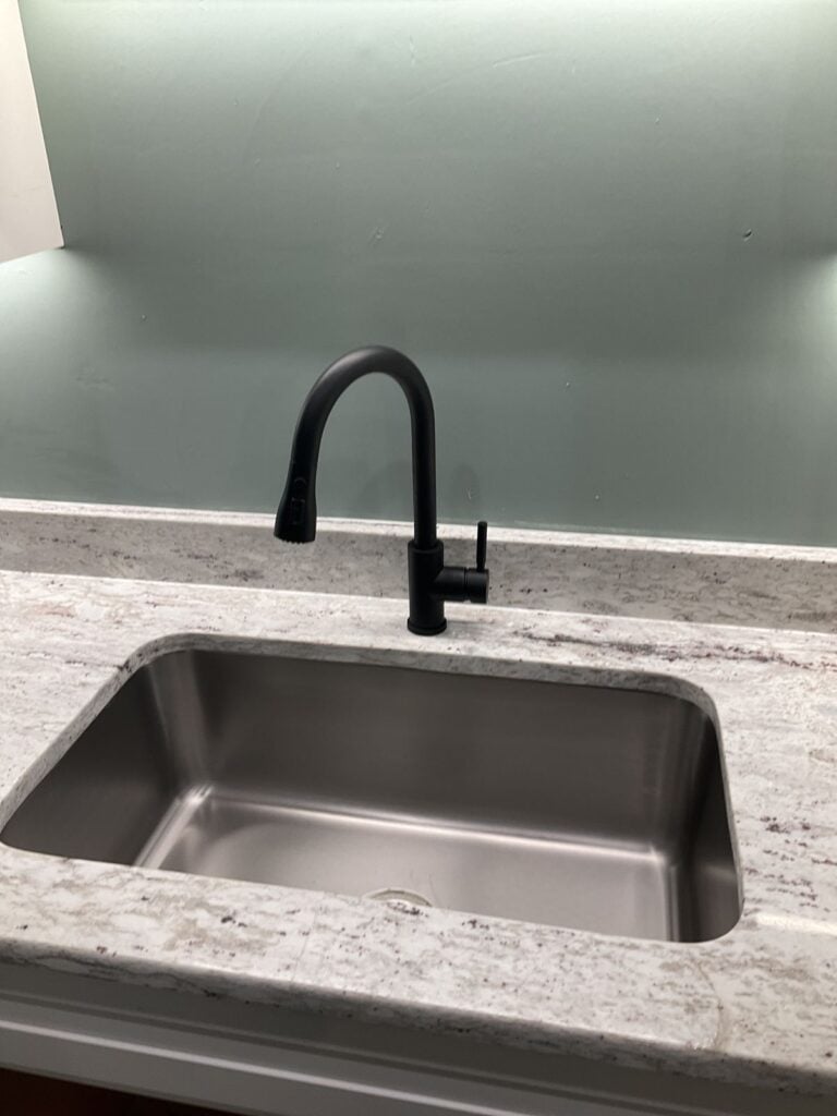 Matte black pull down kitchen faucet on a granite counter above a single bowl undermount stainless sink