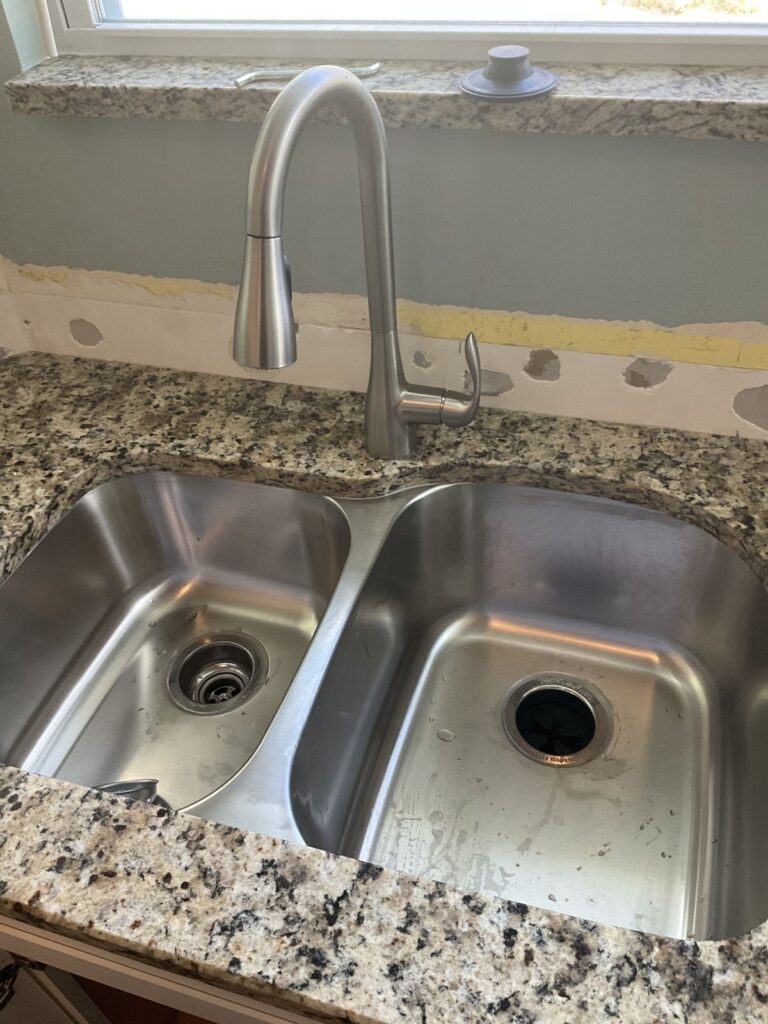 Stainless pull down kitchen faucet on a granite counter above an undermount double bowl sink