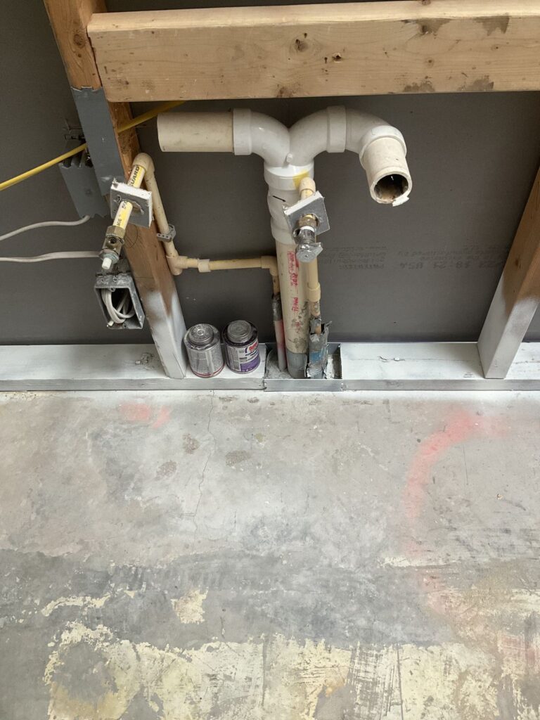 PVC waste stub and yellow gas line roughed into a garage wall frame above a concrete floor