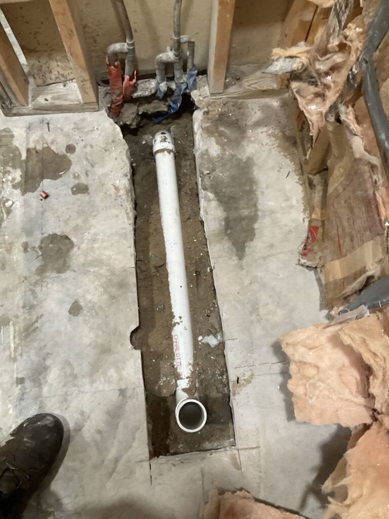 New white PVC drain line laid in a trench cut through a concrete bathroom slab