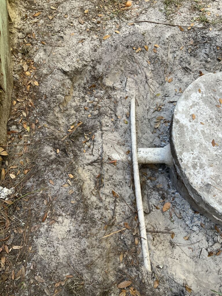 PVC line running through sandy ground beside a round concrete septic tank lid