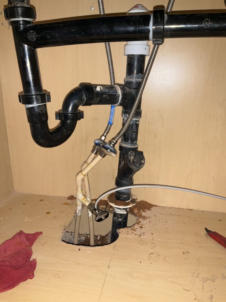 Black ABS sink drain piping above a hole cut in the cabinet floor for the trap arm