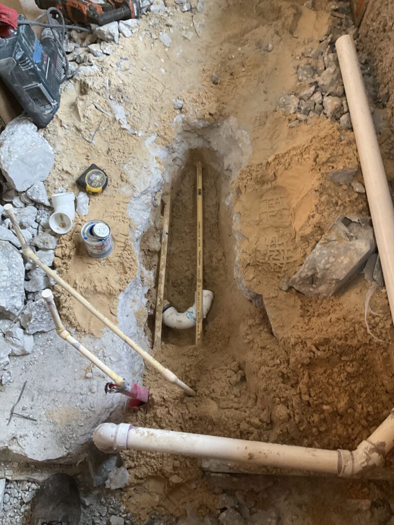 Water lines and a drain elbow in a sand trench cut through a concrete slab