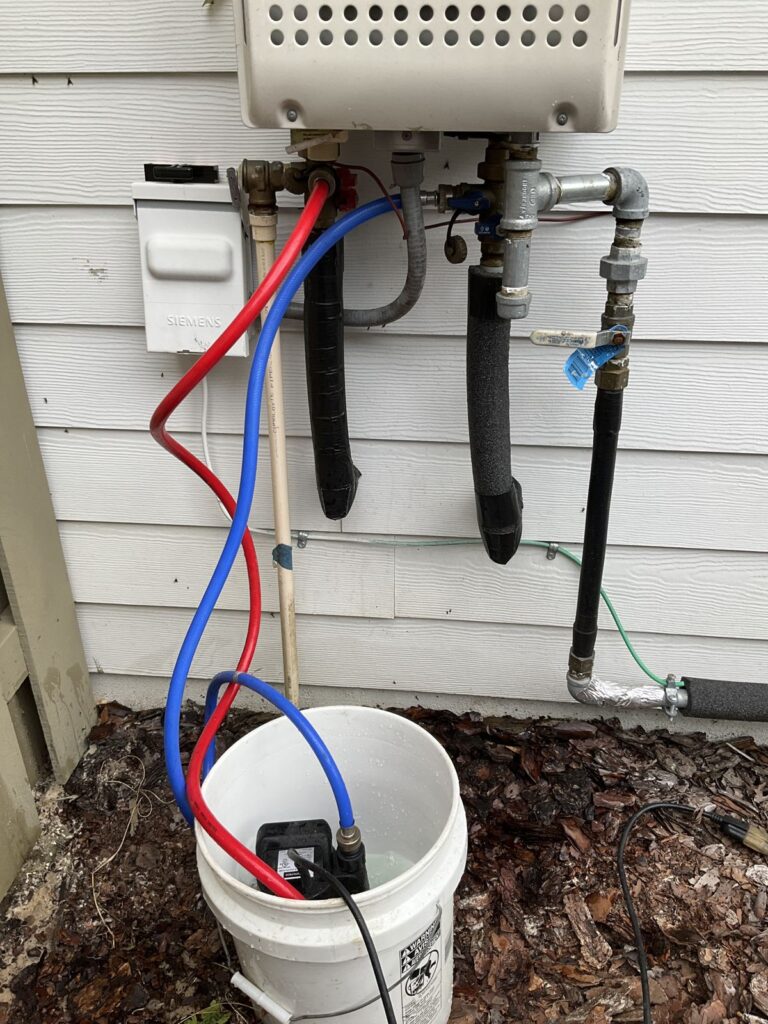Tankless water heater being flushed with red and blue hoses running from the isolation valves to a bucket