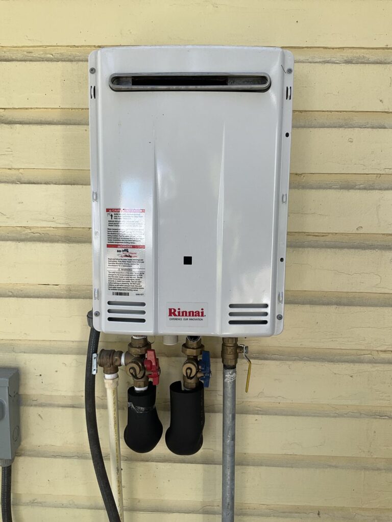 Tankless water heater mounted on exterior siding with isolation valves and the gas line connected