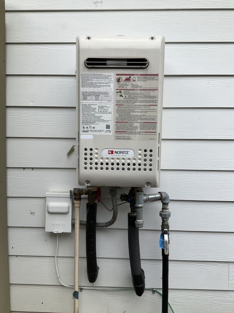 Wall mounted tankless water heater on white lap siding with gas and water connections and isolation valves