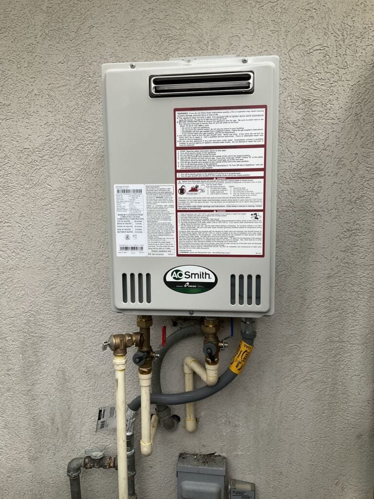 Tankless water heater on an exterior wall with water lines and a gas shutoff below the unit