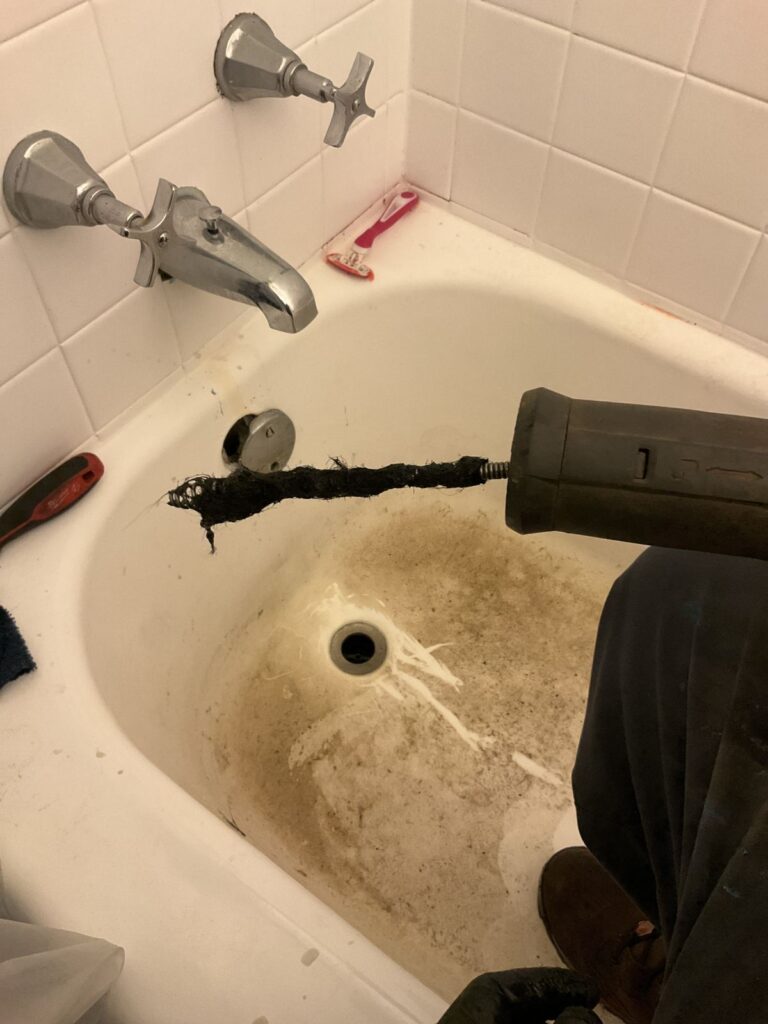 Drain cable pulled out of a tub drain covered in hair and black buildup