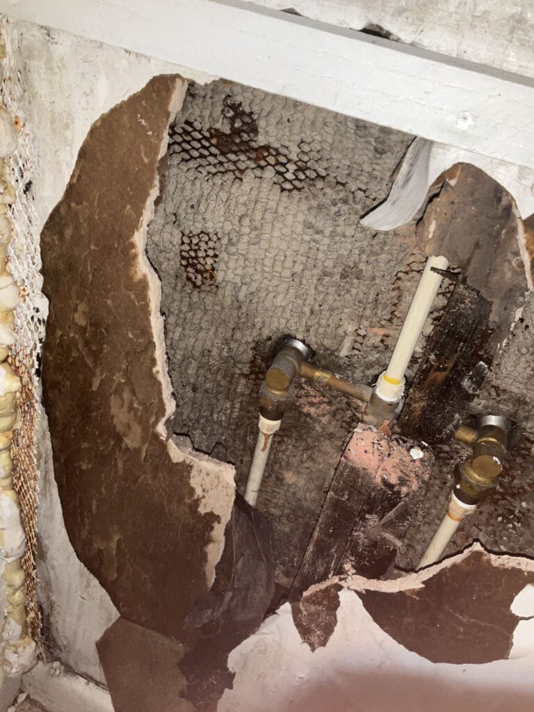 Brass and galvanized valves with CPVC water lines exposed in an opened plaster wall