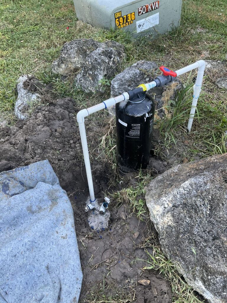 Whole house water filter tank and PVC piping in an excavated yard near a utility transformer