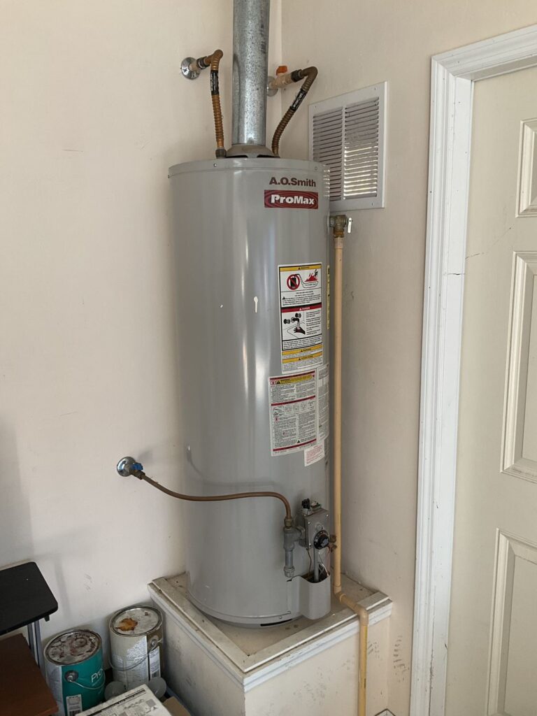 Gas water heater installed on a raised platform with a metal flue and flexible connectors