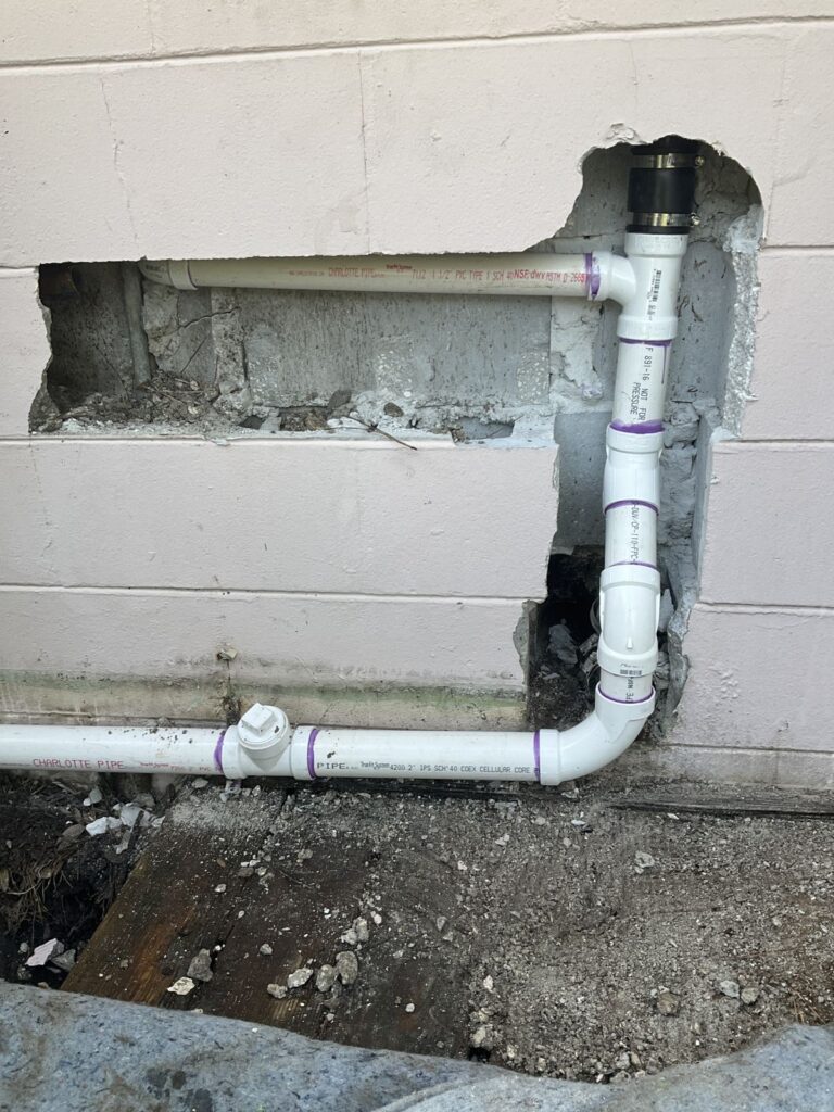 New PVC water line with a brass adapter routed through an opening cut in a block wall