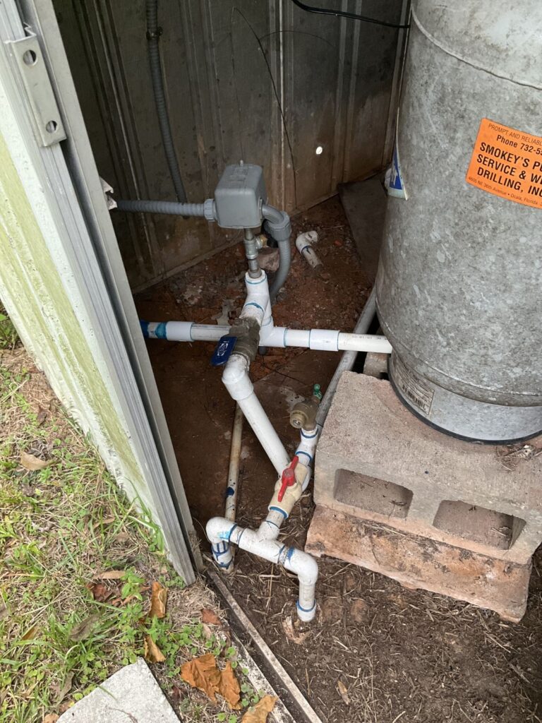 Well pressure tank on blocks in a well house with a PVC manifold, pressure switch and shutoff valves