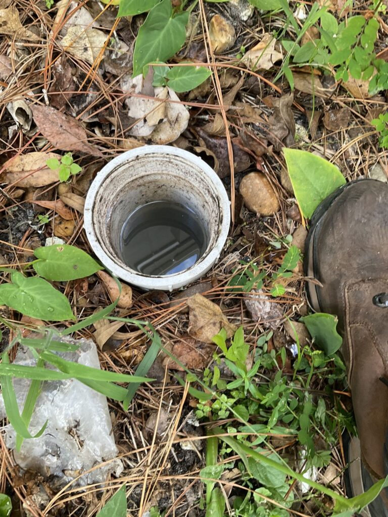 Cleanout pipe in the yard standing full of water next to a work boot