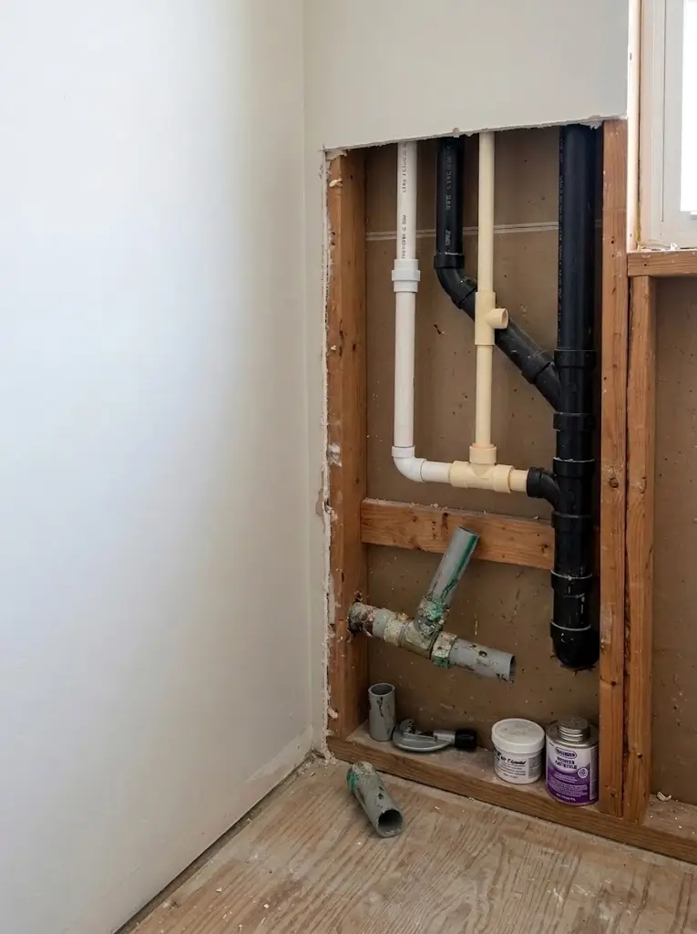 New PVC drain line and vent run inside a bathroom wall opened to the studs
