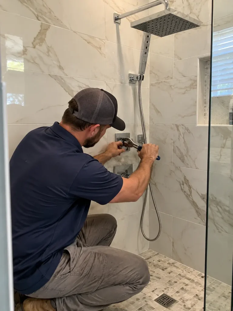 Chrome square rain shower head with a hand shower and two square trim valves on a marble tiled wall